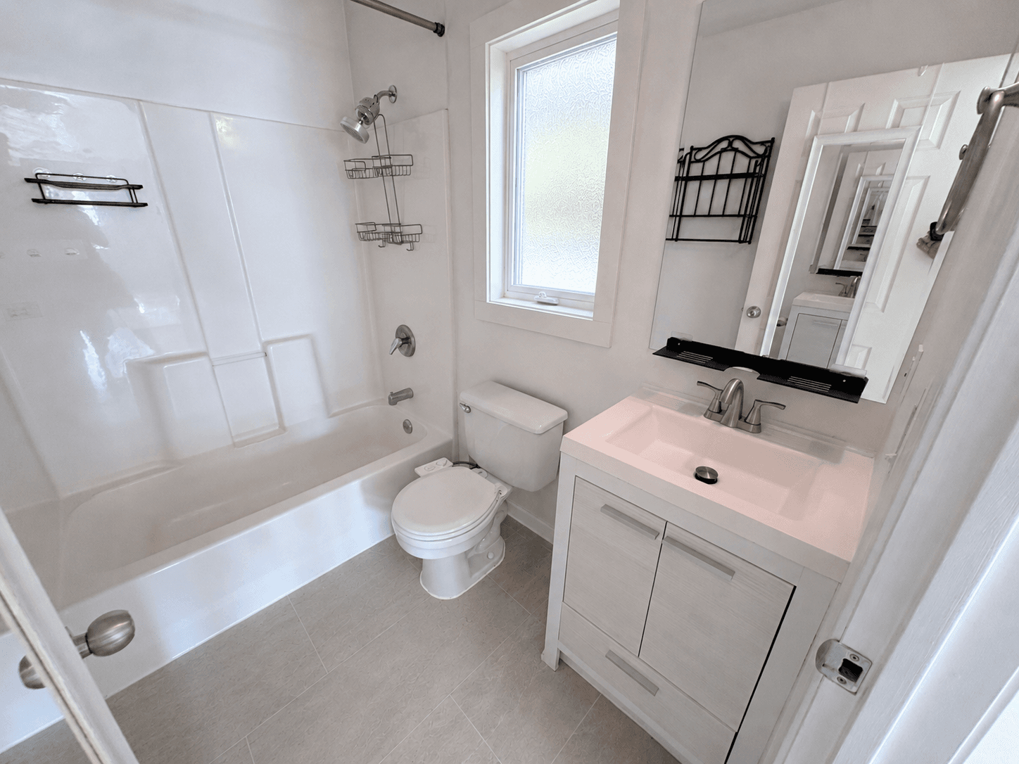 Bright white bathroom featuring a bathtub, toilet, and vanity with a large wall mirror.