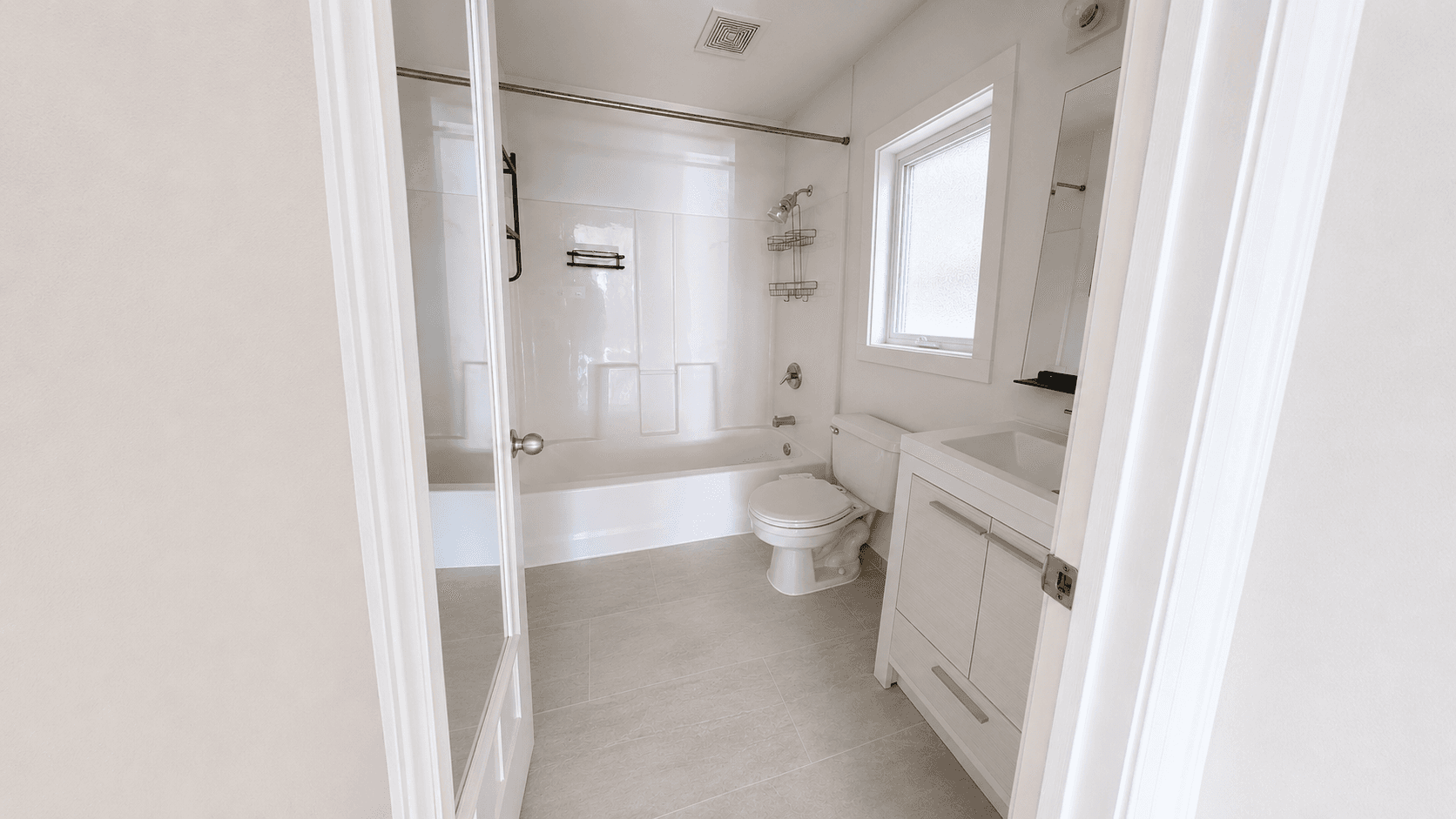 Modern white bathroom with a bathtub, toilet, and vanity, viewed through an open doorway.