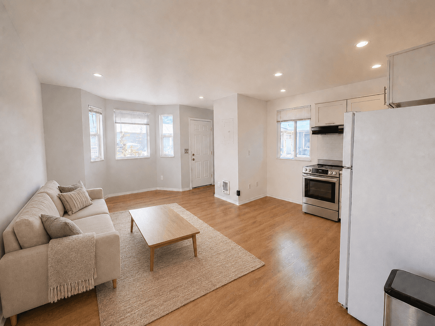 Bright open-concept living area with beige sofa, wooden coffee table, and stainless steel appliances.