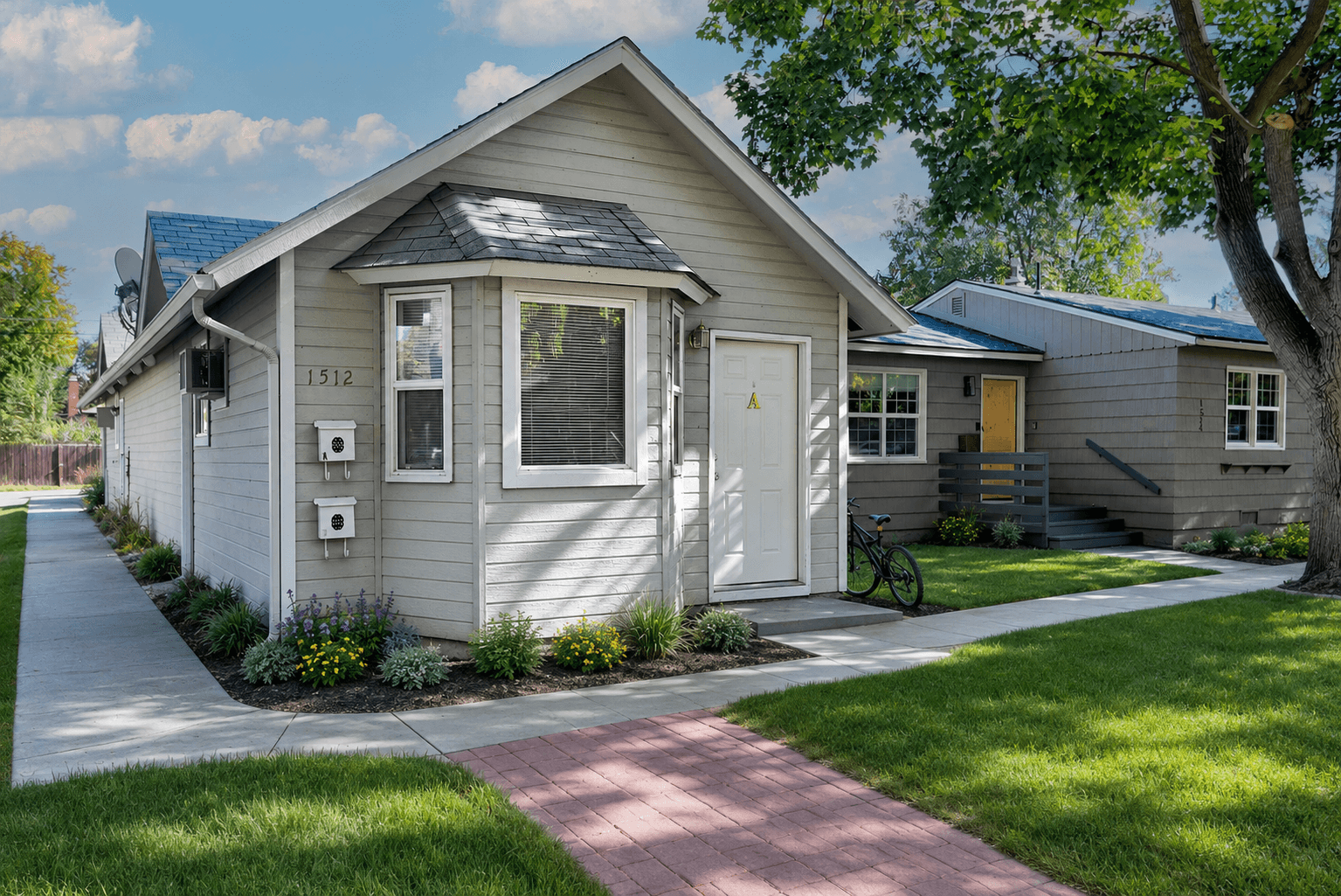 Light gray house with a bay window, white door, and flowers along the sidewalk.