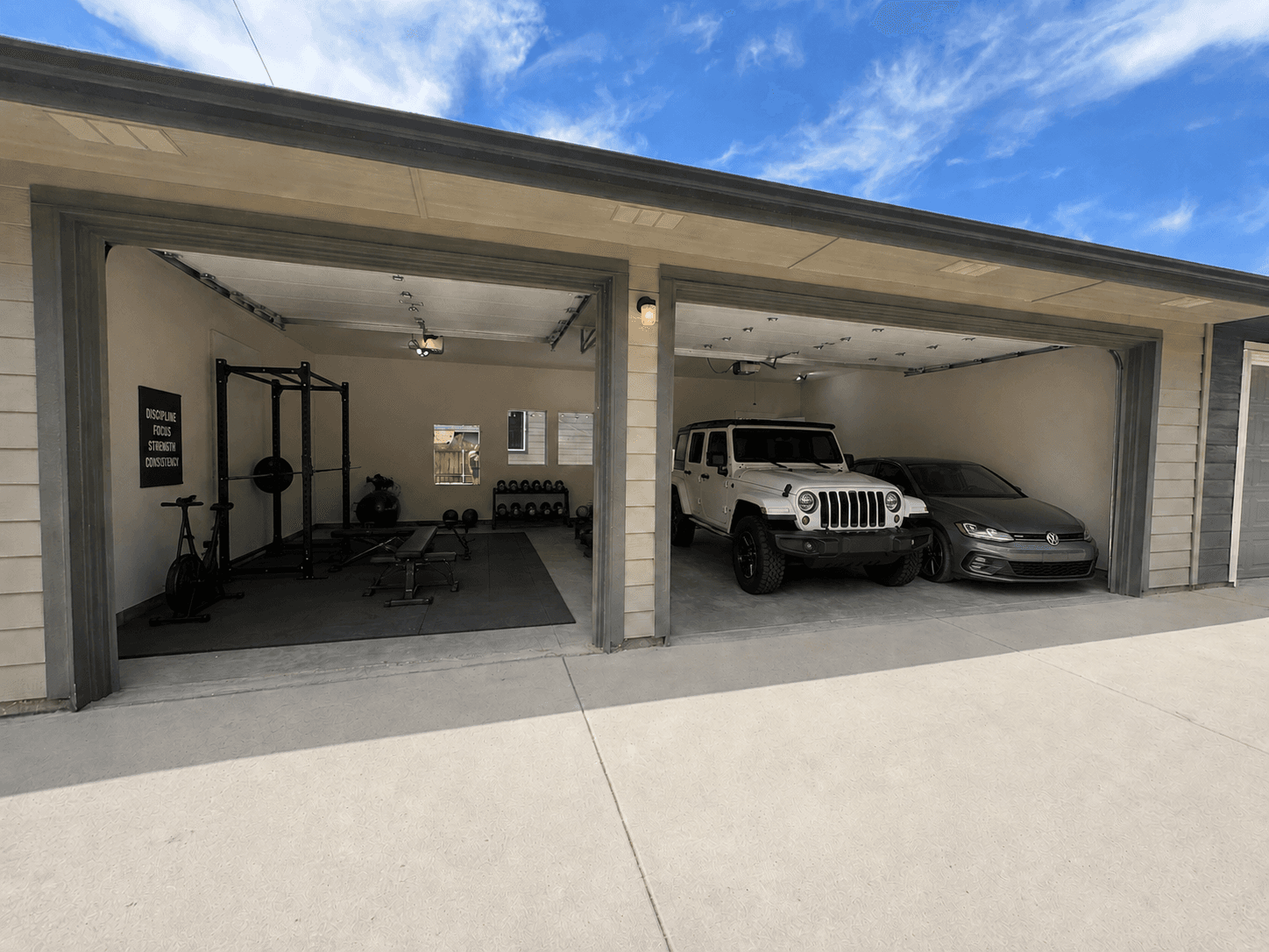 Open garage with home gym on left, white Jeep and grey car on right.