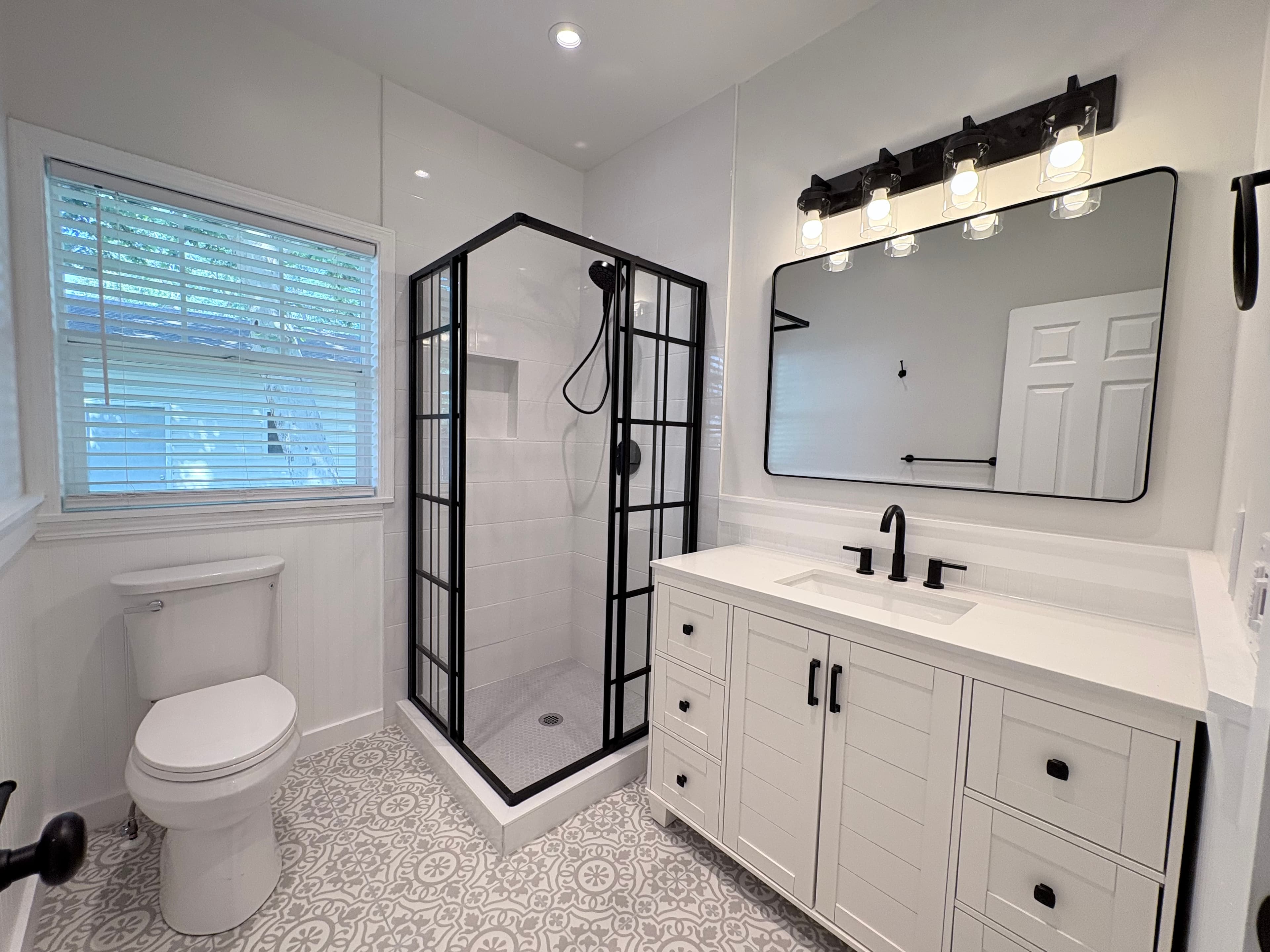 Modern bathroom featuring a black grid shower, white vanity, and intricate gray patterned floor tiles.