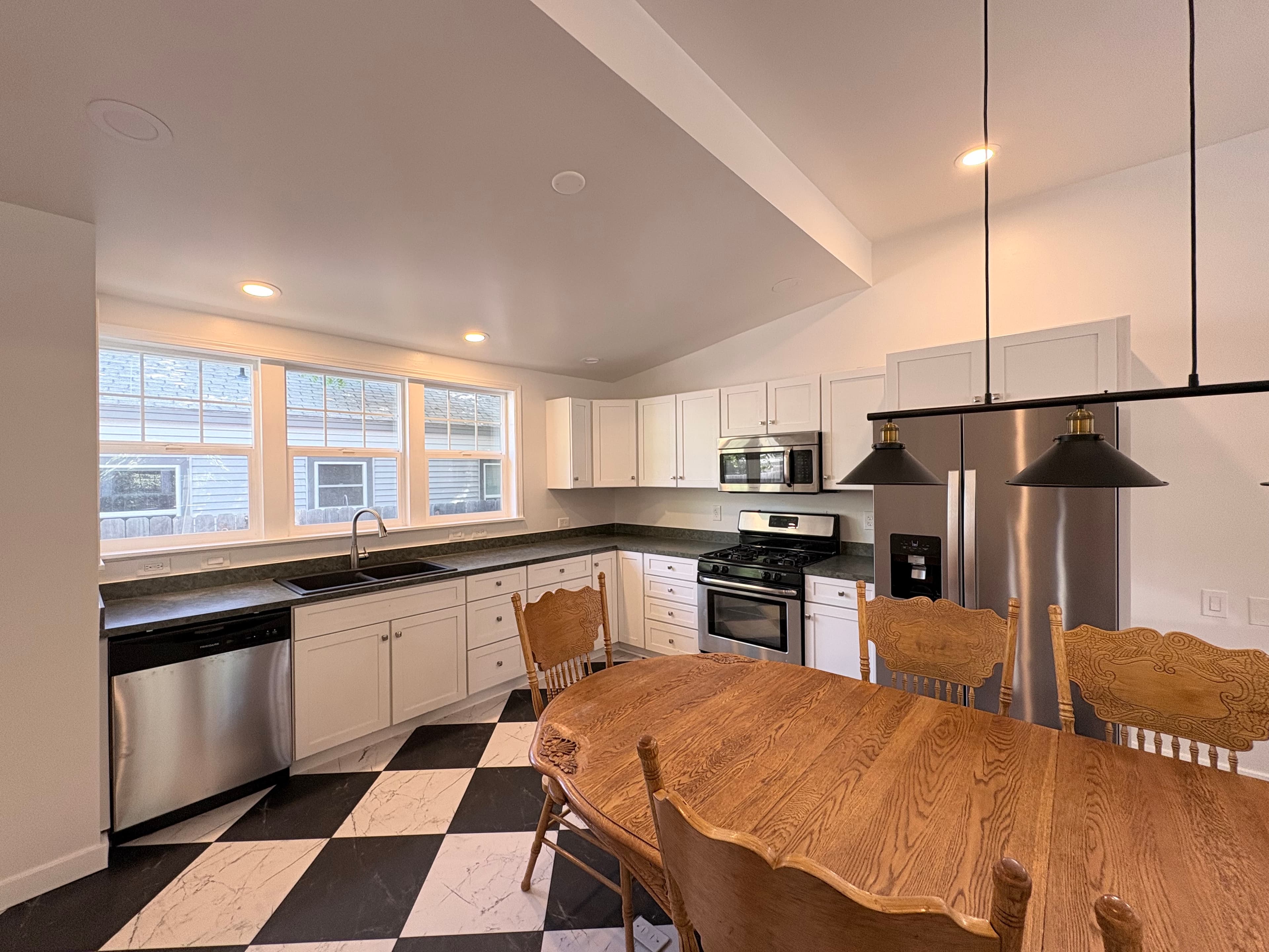 Bright kitchen with white cabinets, checkered floor, stainless appliances, and a wooden dining table.