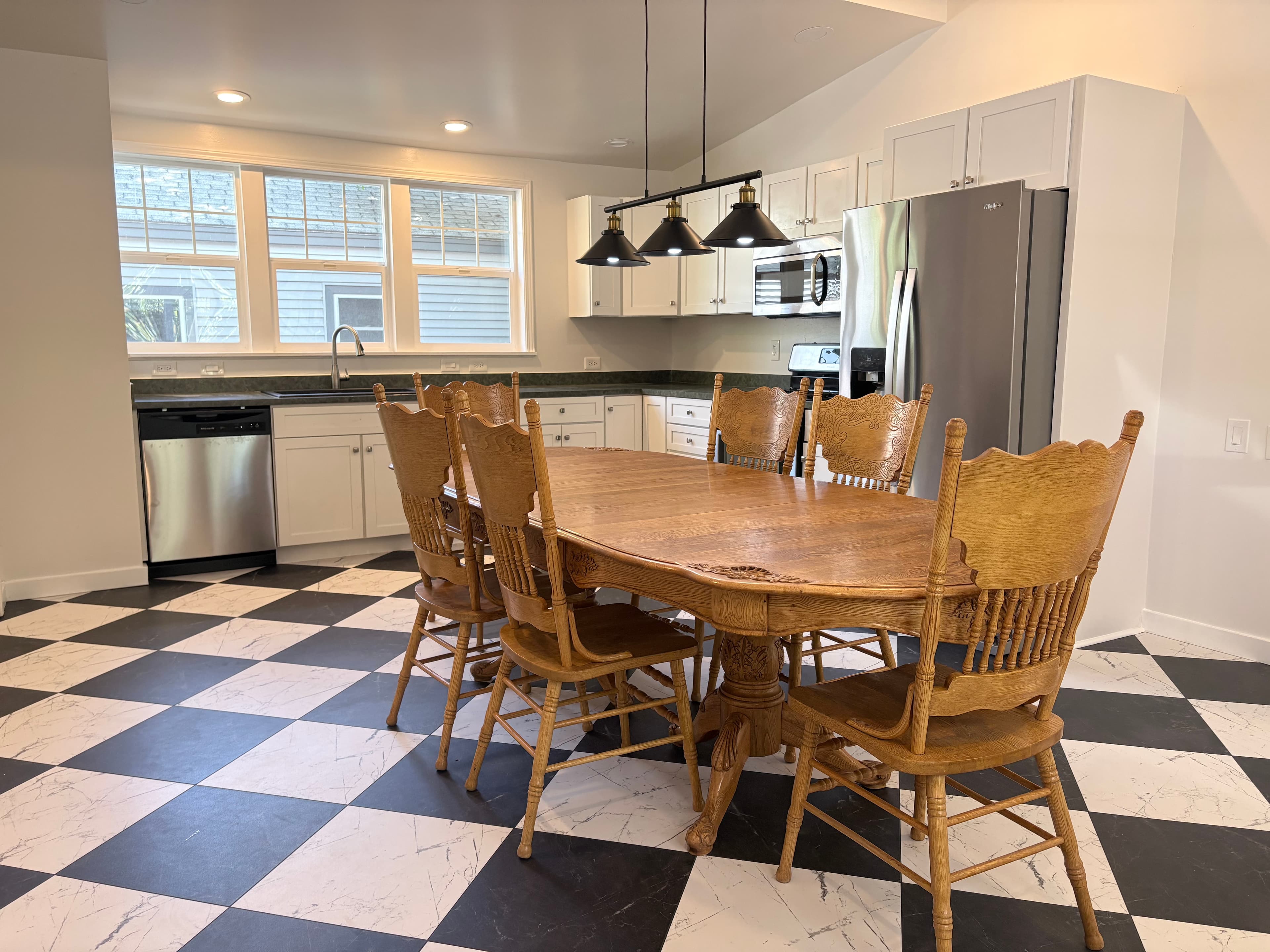 Light-wood dining set on a black and white checkered floor in a modern kitchen.